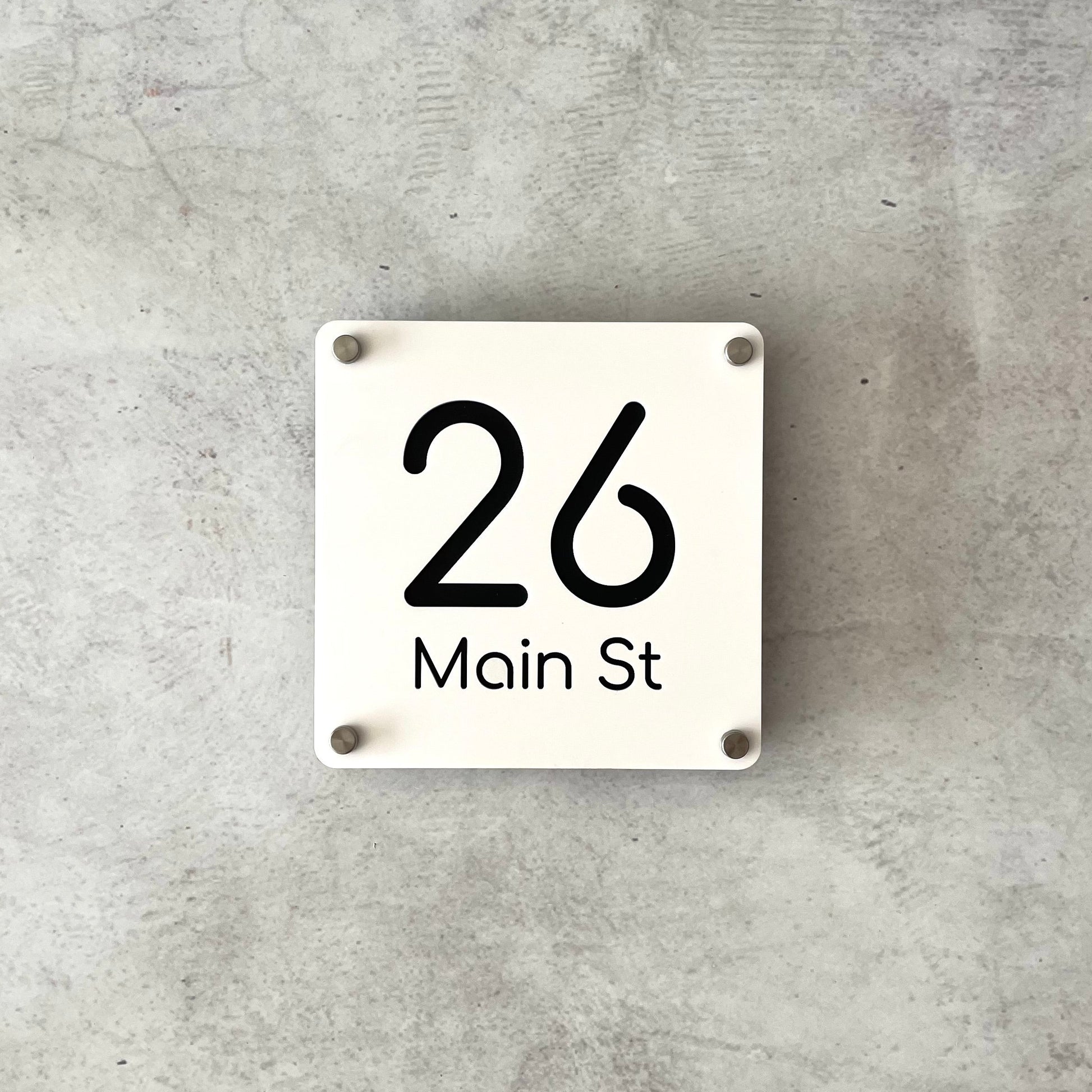 White square house number sign on a grey concrete background with standoff mounts