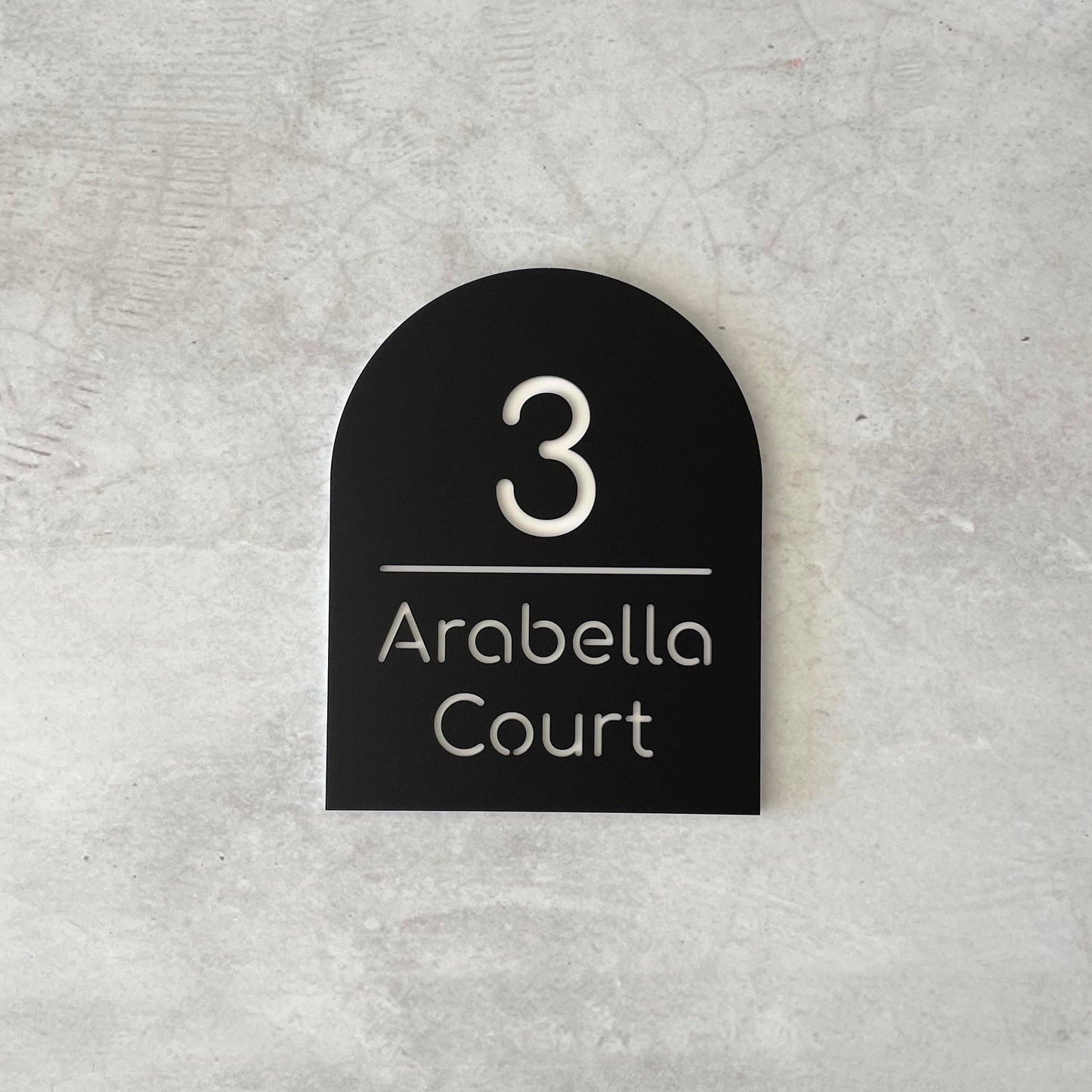 Black arch-shaped house number sign grey concrete background