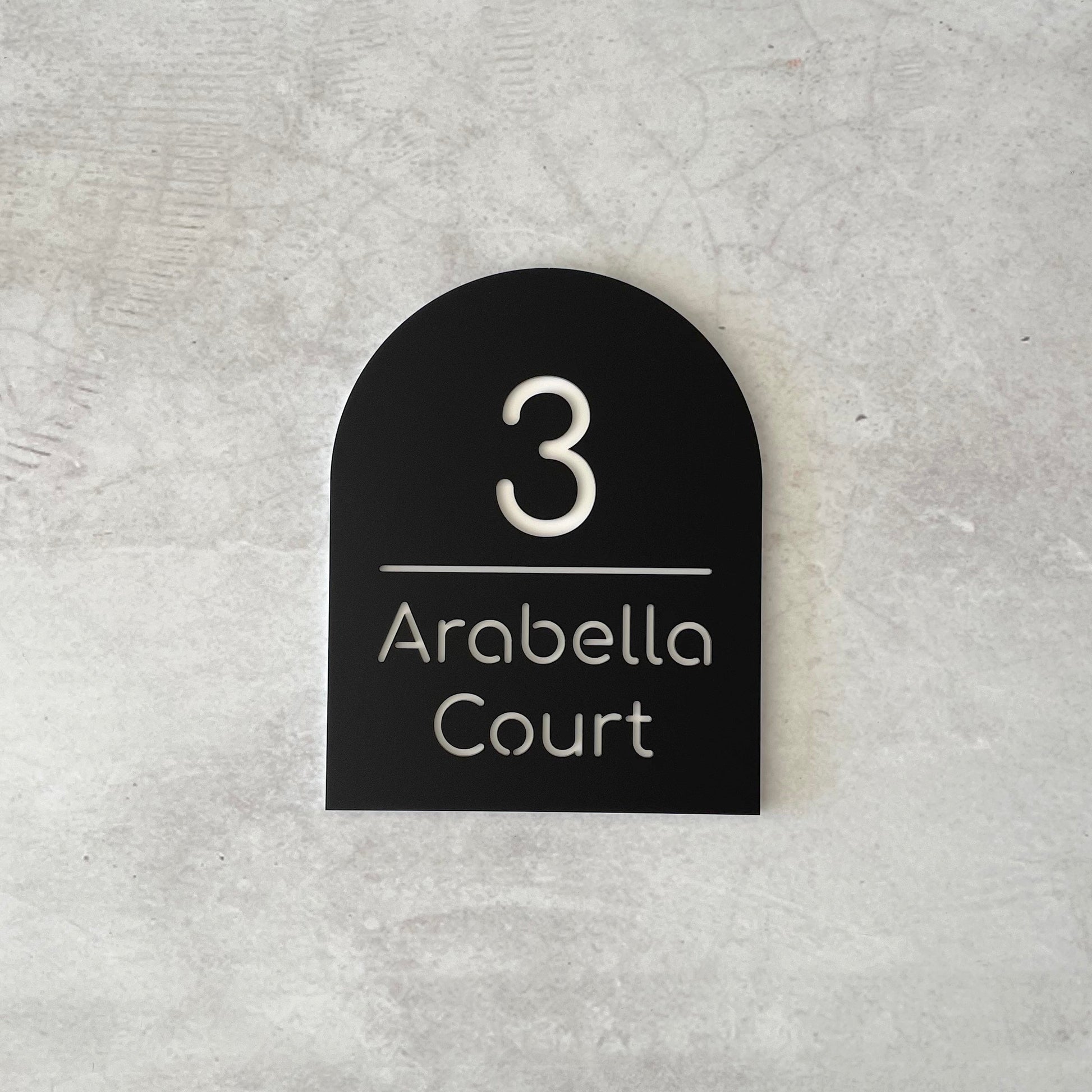 Black arch-shaped house number sign grey concrete background