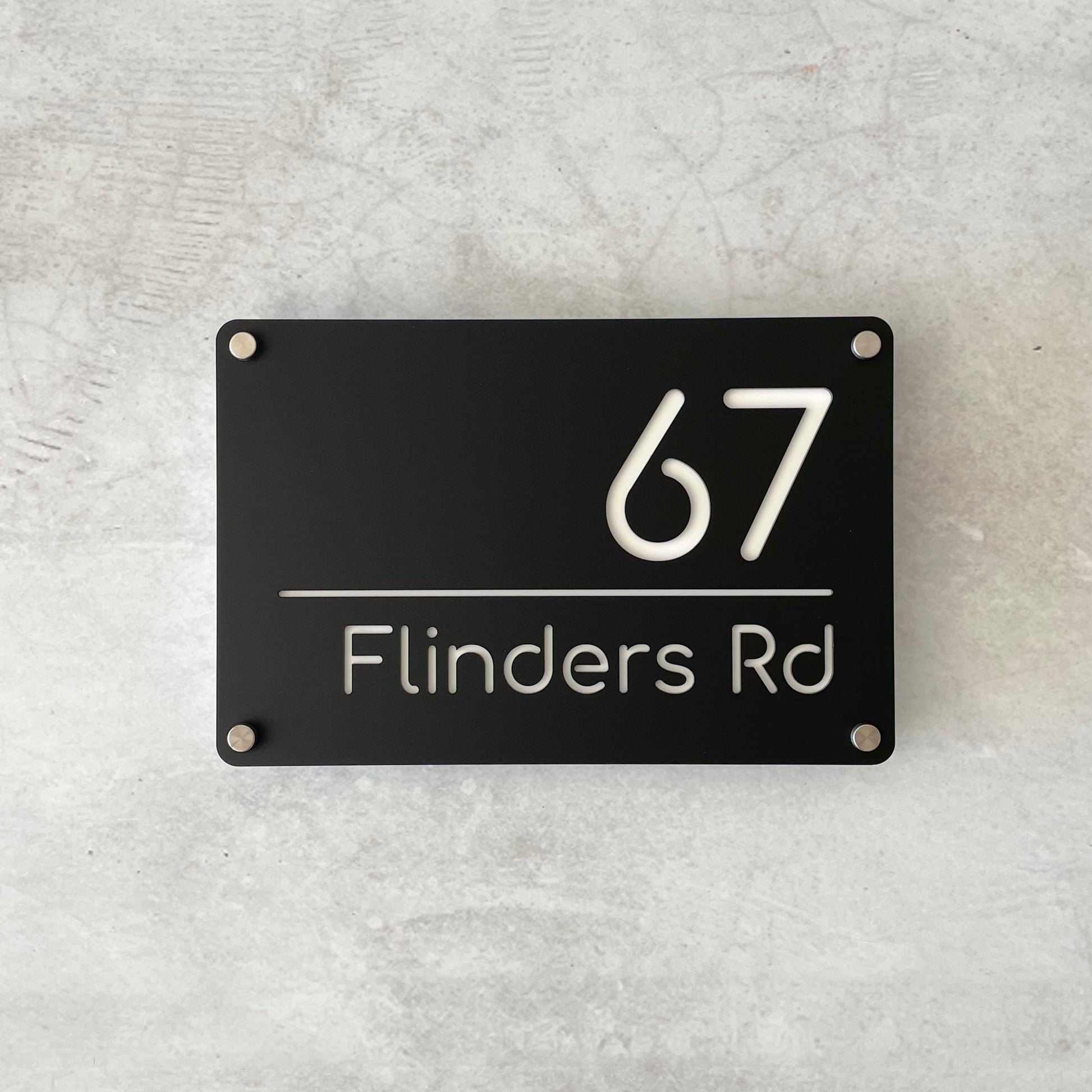 Black rectangular address sign with white text on a grey textured background