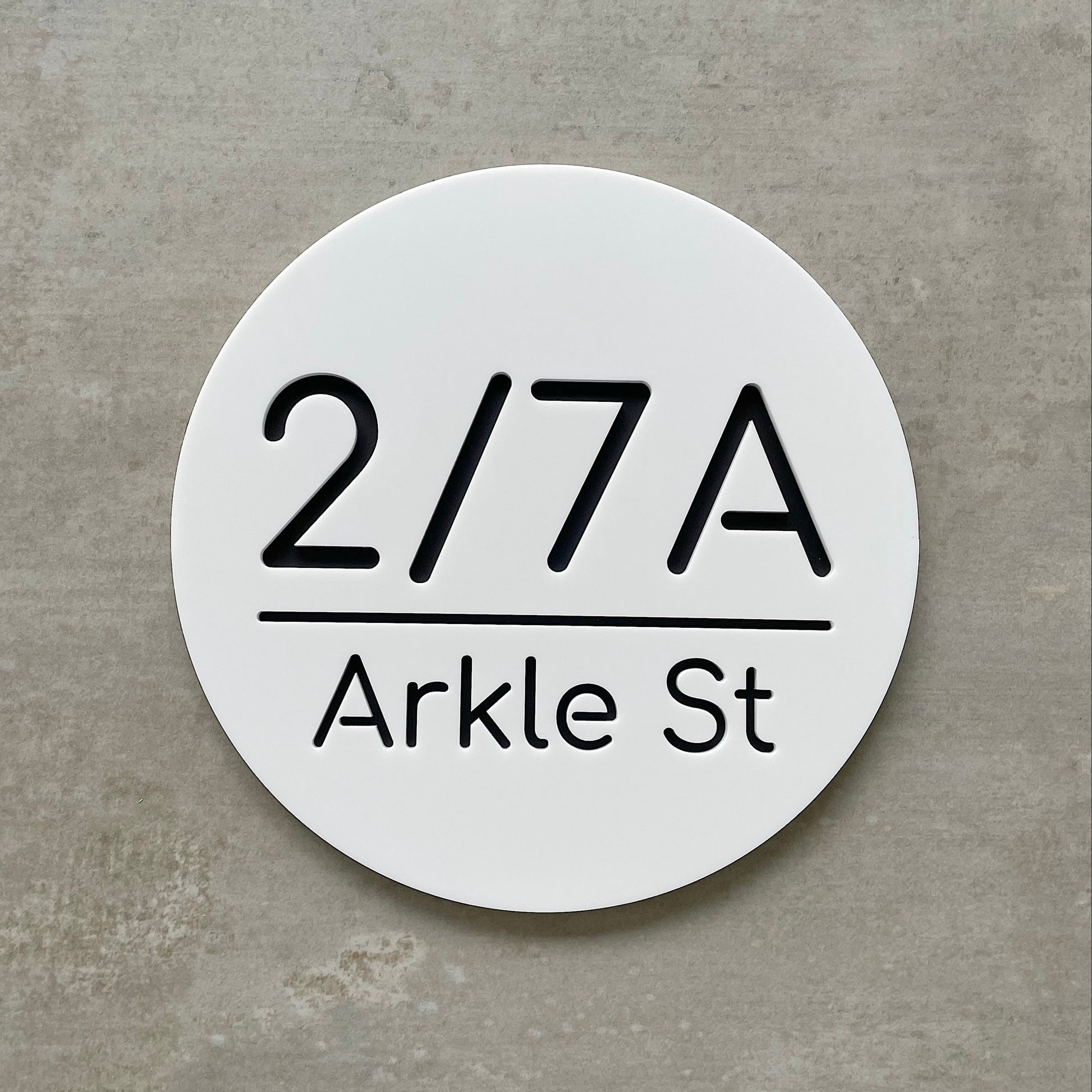 Round white house number sign with black text on a concrete background