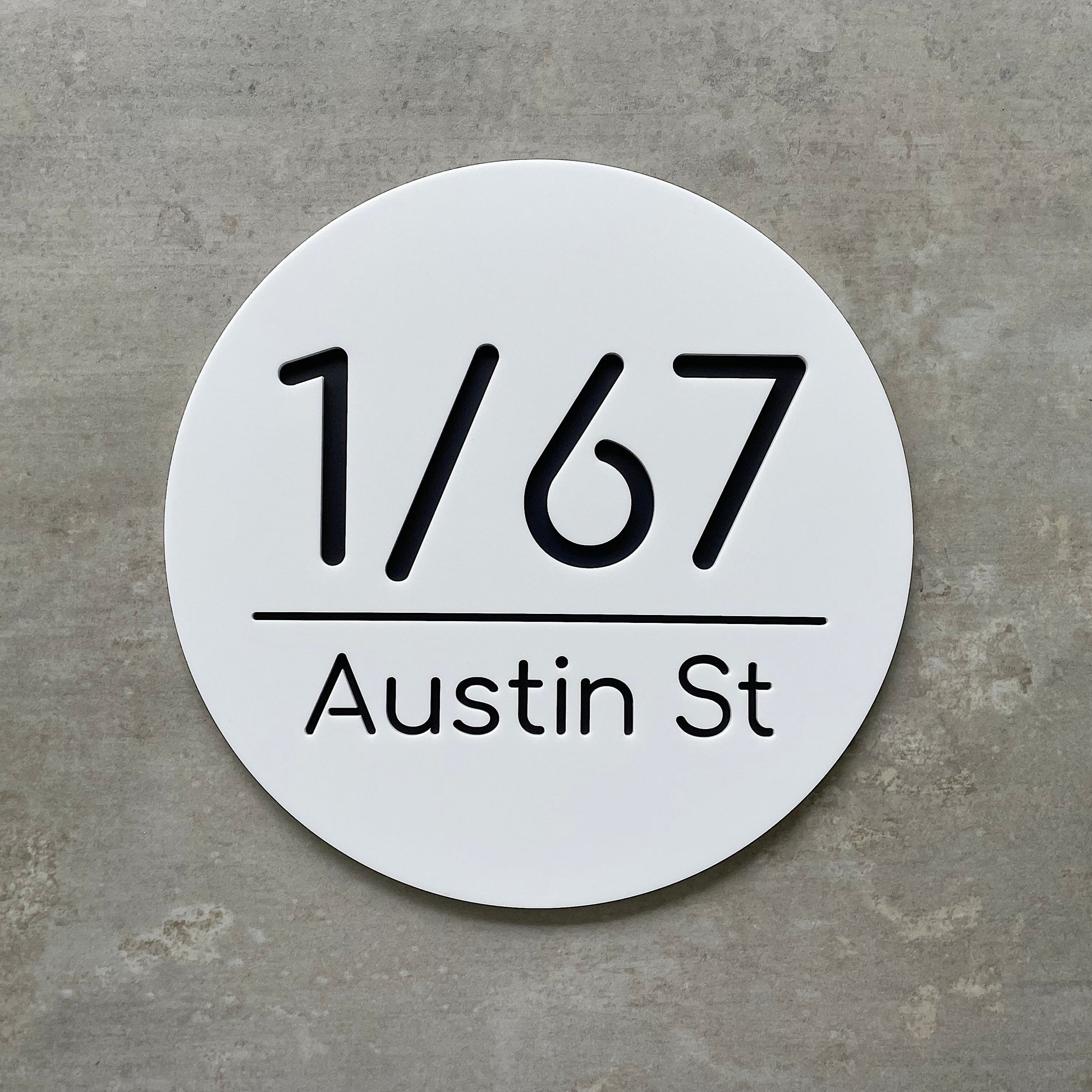 Round white house number sign with black text on a concrete background