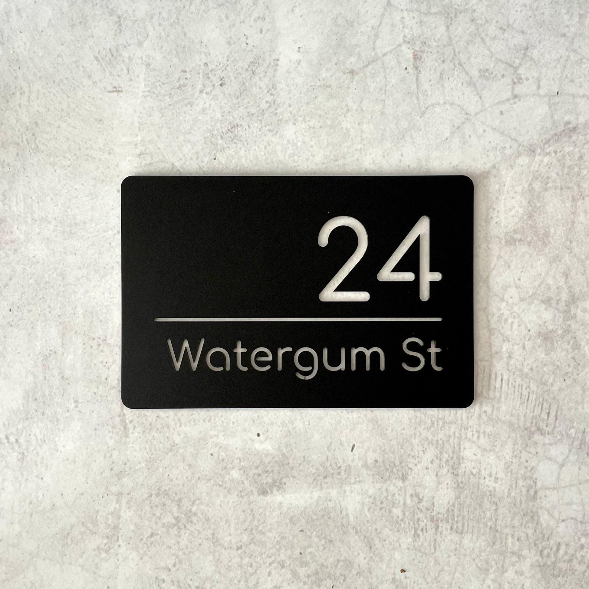 Single layer black rectangular house number plaque with modern font, lettering cutout to reveal wall behind