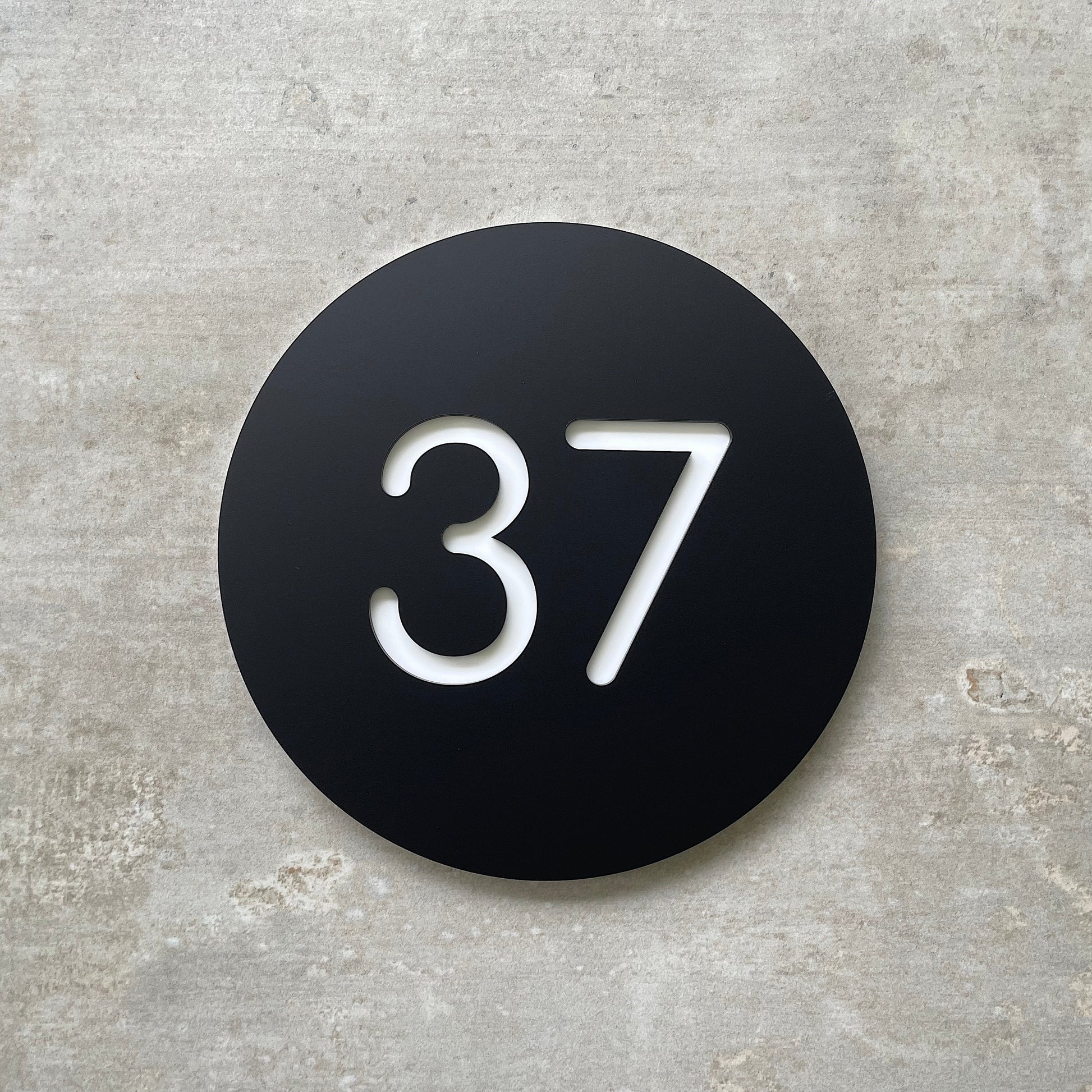Modern black circular house number sign with the number 37 in white.