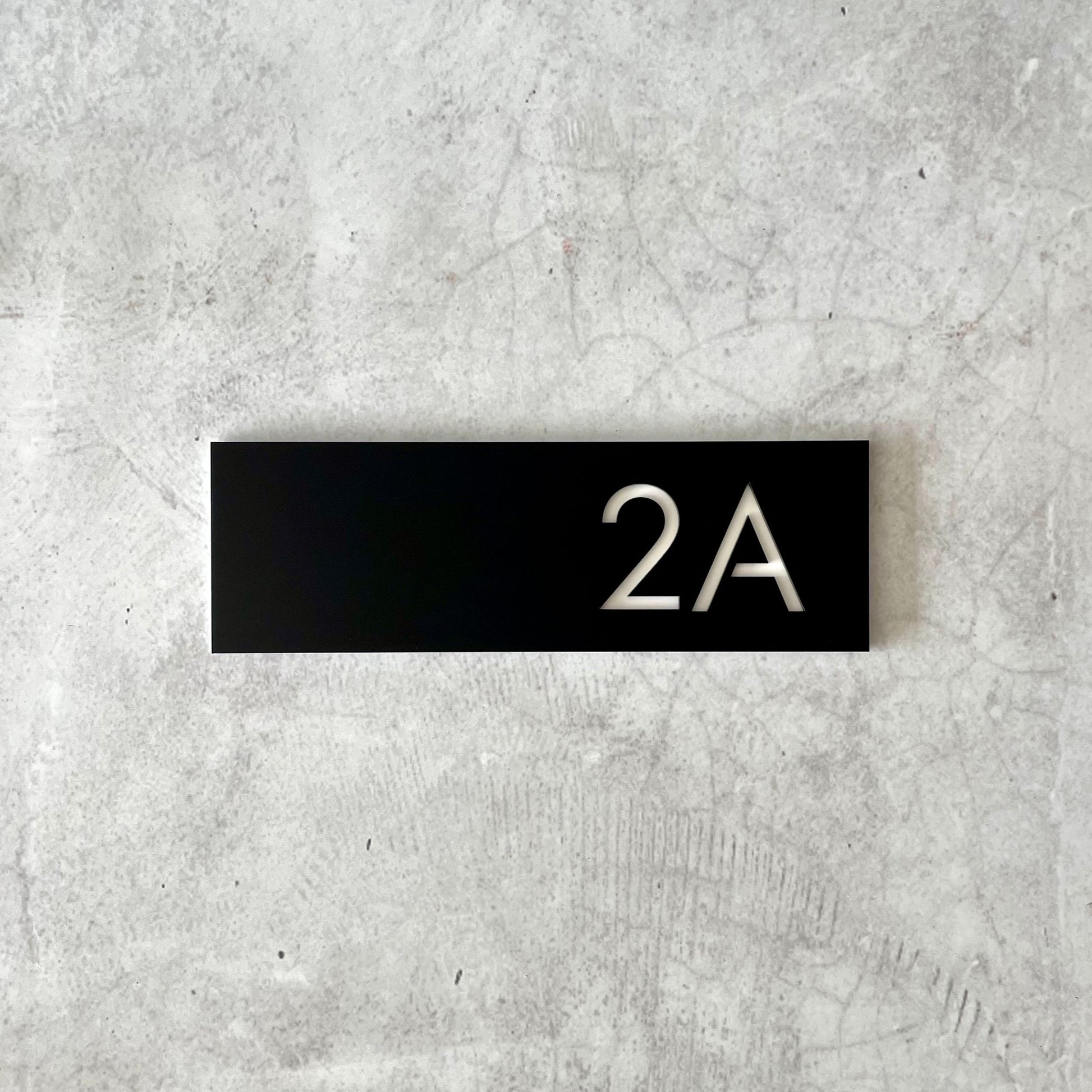 Black rectangular house number with '2A' on a textured grey background