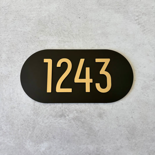 Black oval sign with brushed gold unit numbers