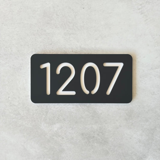 Charcoal rectangular plate with white apartment numbers '1207' on a light gray background