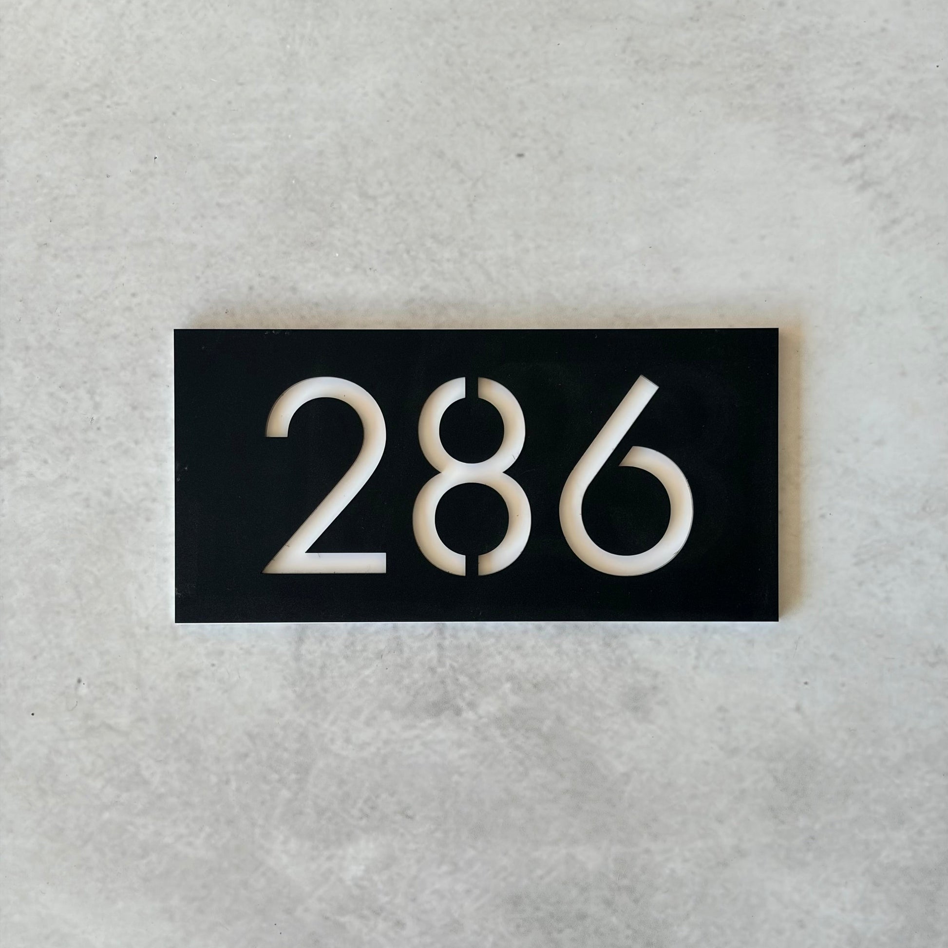 Black rectangular plate with white unit numbers on a grey background