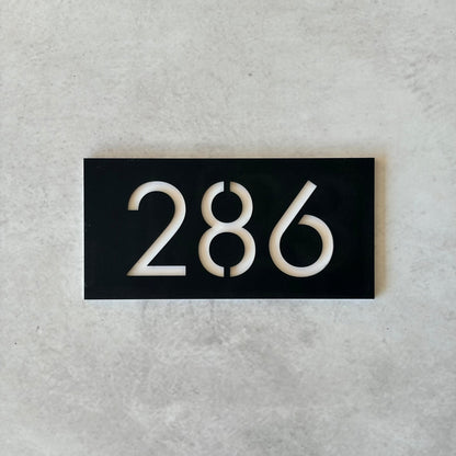 Black rectangular plate with white unit numbers on a grey background