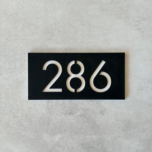Black rectangular plate with white unit numbers on a grey background