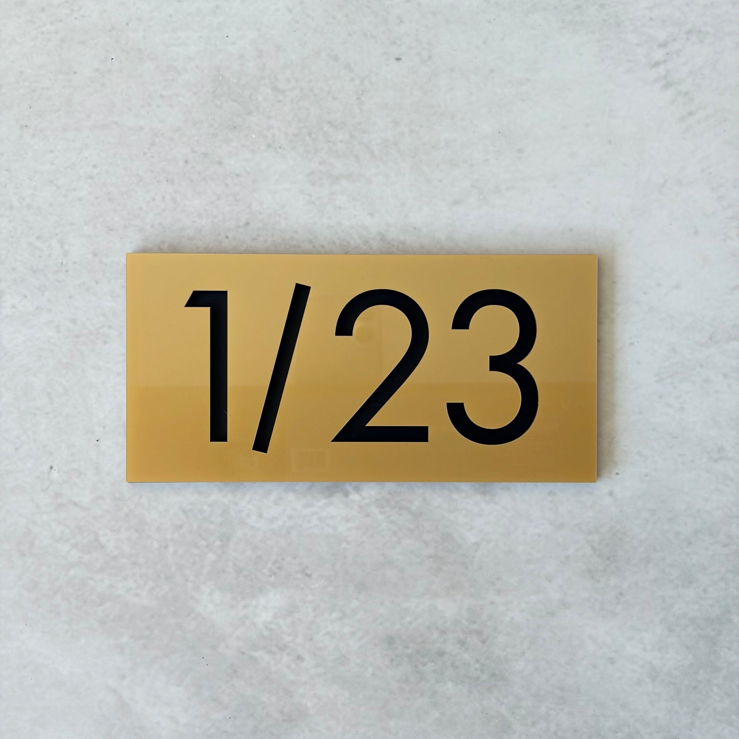 Gold plaque with black unit number '1/23' on a light grey background