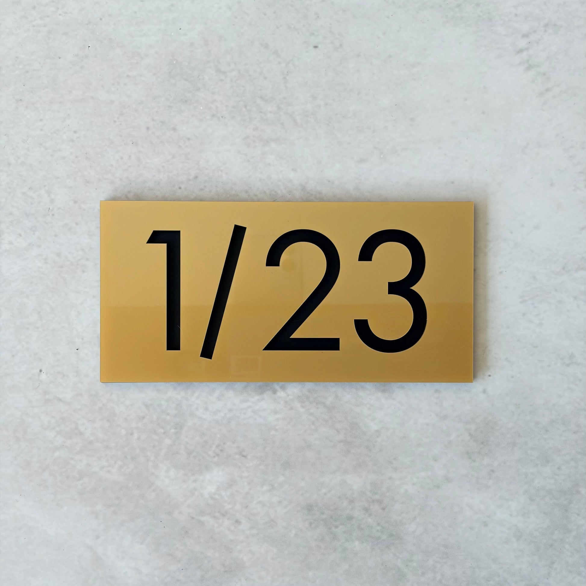 Gold plaque with black unit number '1/23' on a light grey background