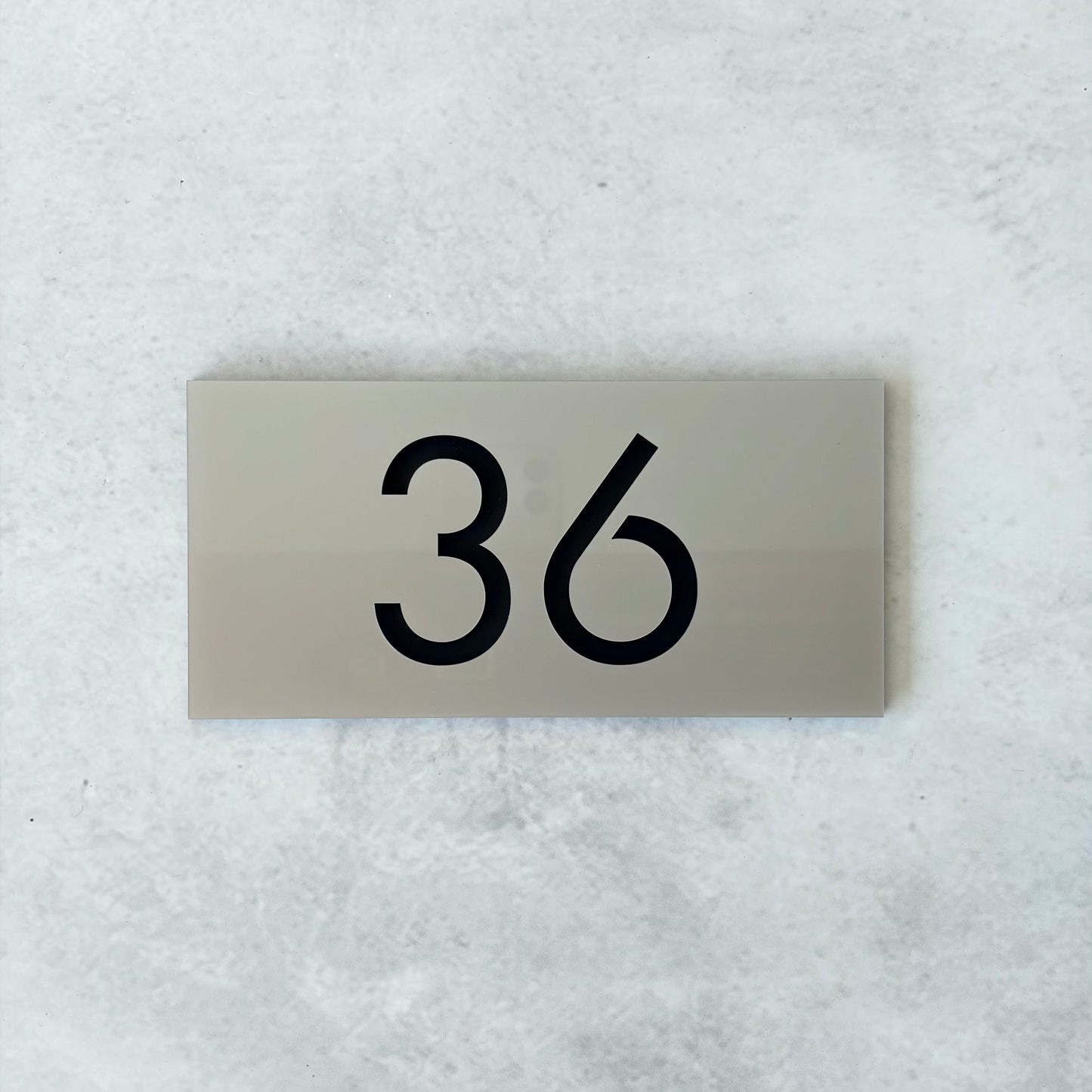 Metallic silver unit number plate with '36' on a textured white background