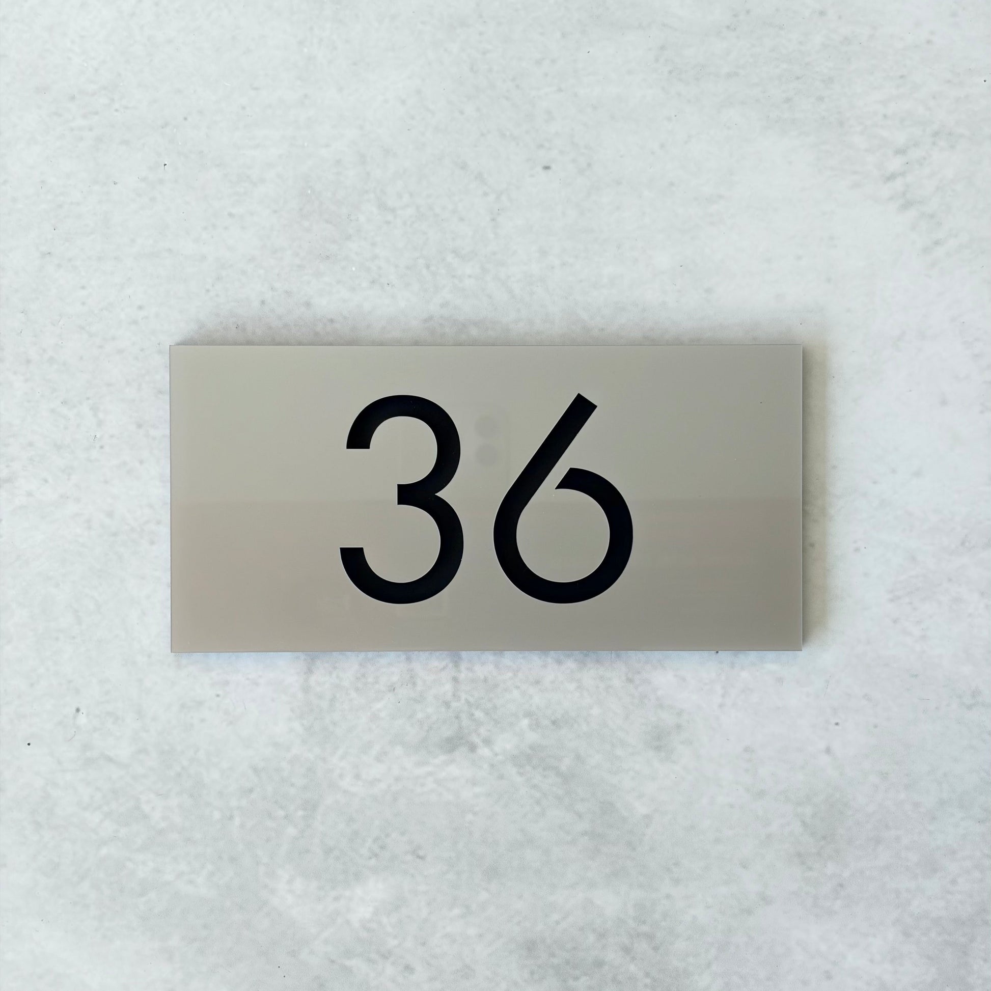 Metallic silver unit number plate with '36' on a textured white background