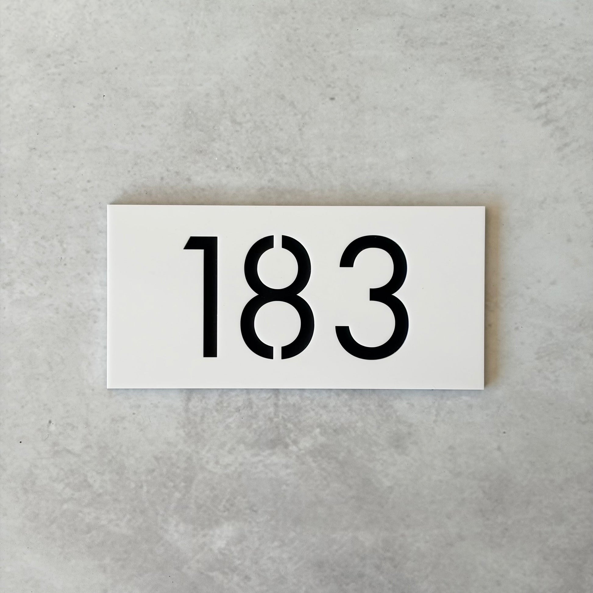 White apartment sign with black numbers '183' on a grey concrete background