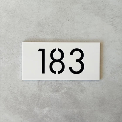 White apartment sign with black numbers '183' on a grey concrete background