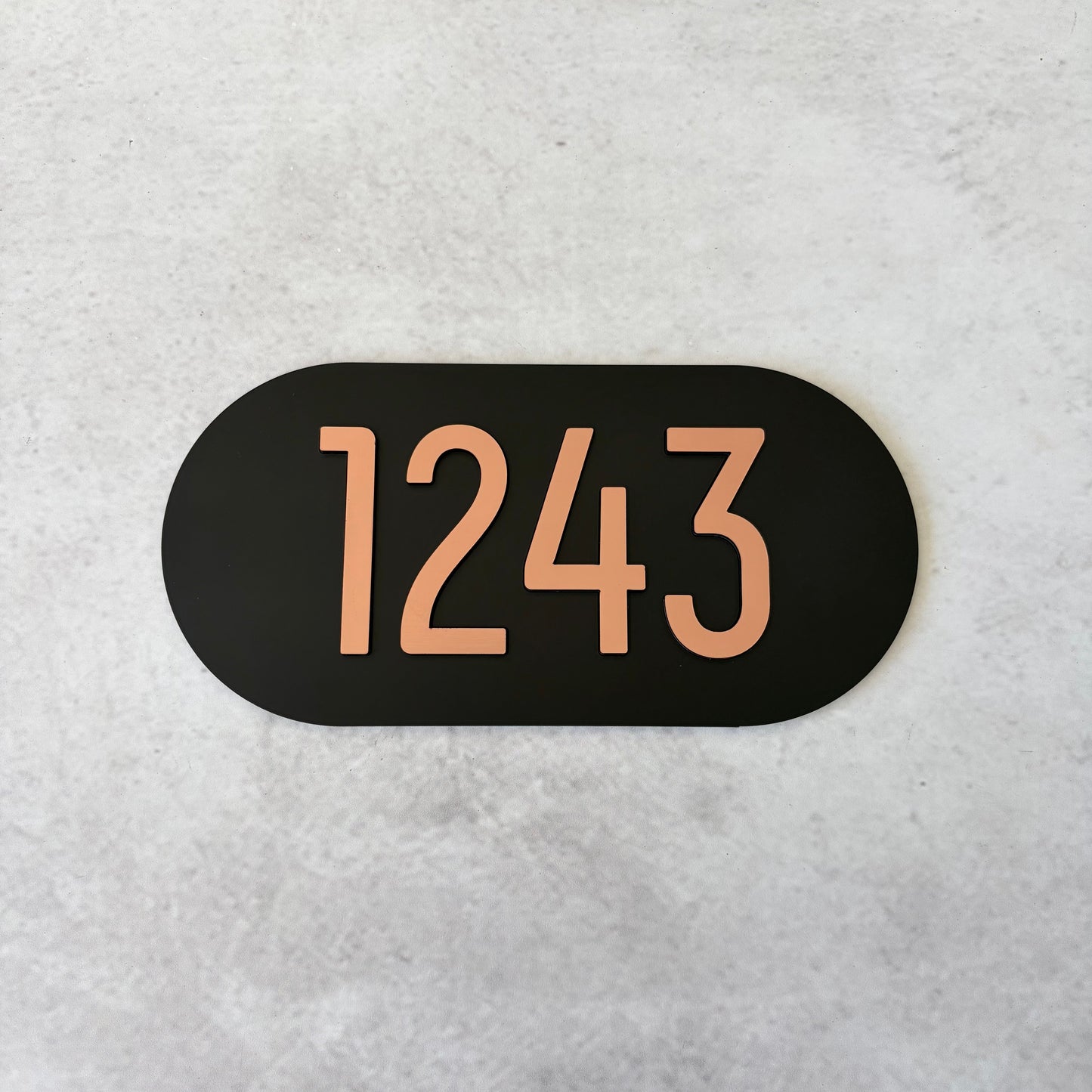 Black oval sign with brushed copper unit numbers on a light grey background