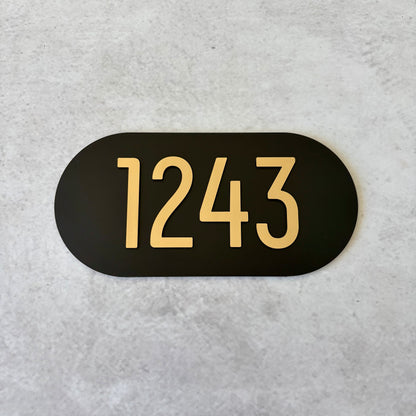 Black oval sign with brushed gold unit numbers