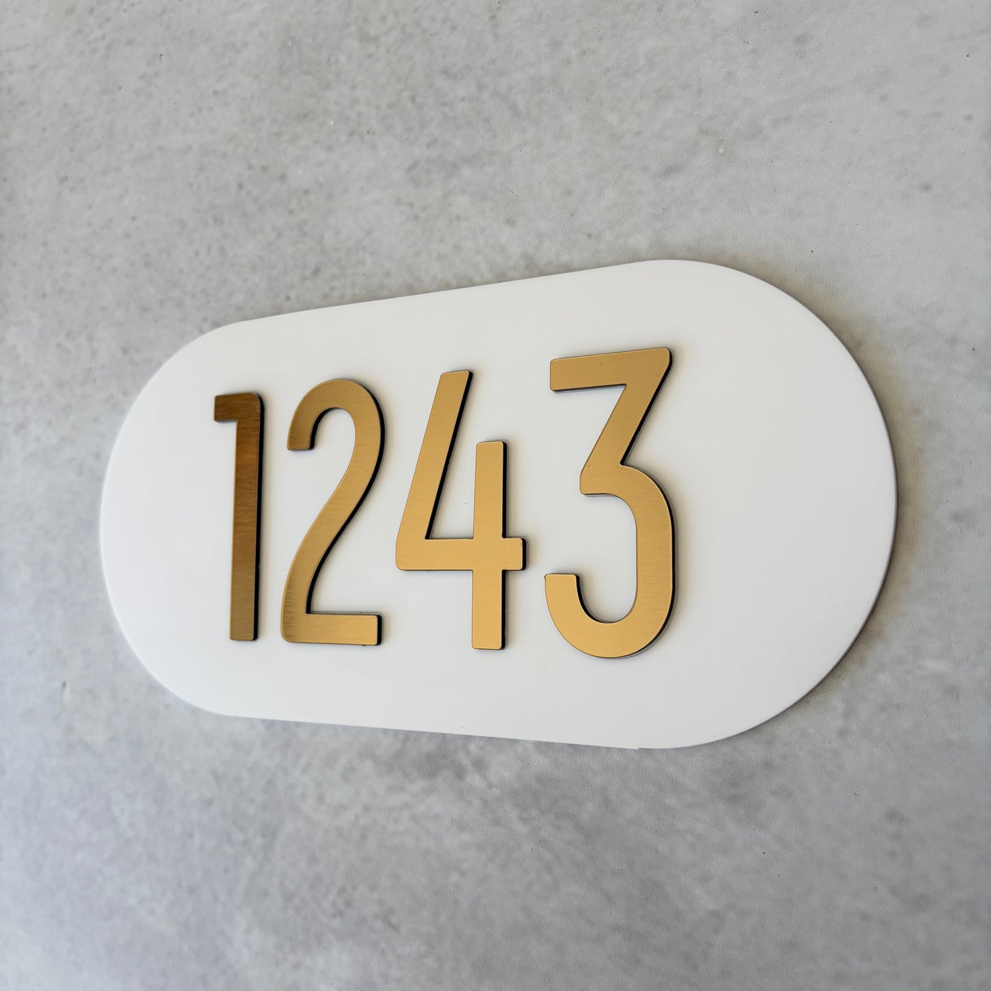 White oval plaque with brushed gold unit numbers '1243' on a grey background