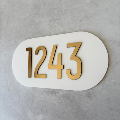 White oval plaque with brushed gold unit numbers '1243' on a grey background